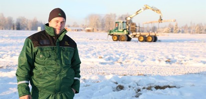 Opiskelija poseeraa metsäkoneen edessä.