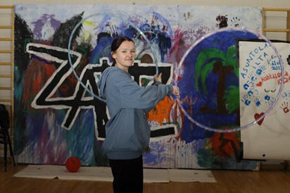 Kuvassa Kälviä Artsin opiskelija Henna Hietamäki seisoo graffitiseinän edessä kahta hulavannetta käsissään pidellen.