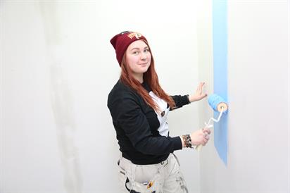 Kuvassa opiskelija maalaa seinää telalla