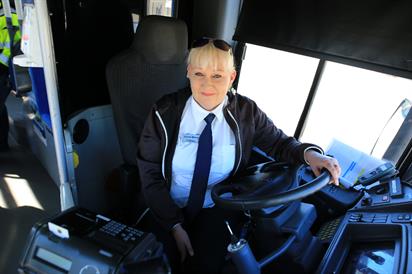 Kuvassa linja-autokuskiksi valmistunut Tarja Partanen poseeraa auton ratissa istuen.