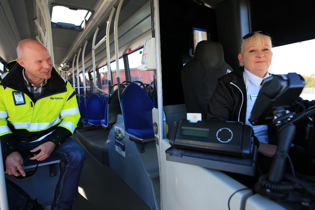 Kuvassa linja-autonkuljettajaksi valmistunut Tarja Partanen poseeraa auton ratissa. Vieressä istuu kouluttaja Jussi Männistö. 