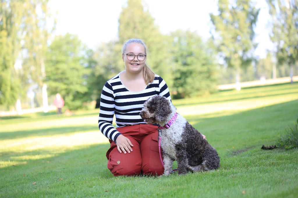 Kuvassa kennelalan opiskelija Siiri Kaskinen poseeraa koiransa kanssa ulkona istuen.