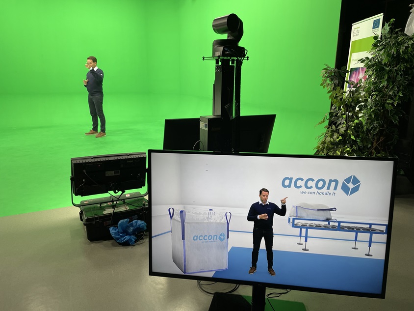 Accon Suomi Oy Etualalla monitori, jossa tuote-esittelijä on virtuaalitodellisuudessa. Taustalla sama esittelijä green screenin edessä.