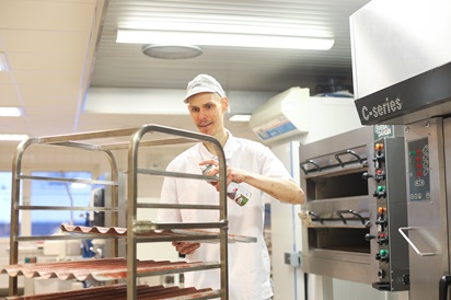 Kuvassa opiskelija Sauli Kangas laittaa leipomossa öljyä patonkipeltiin