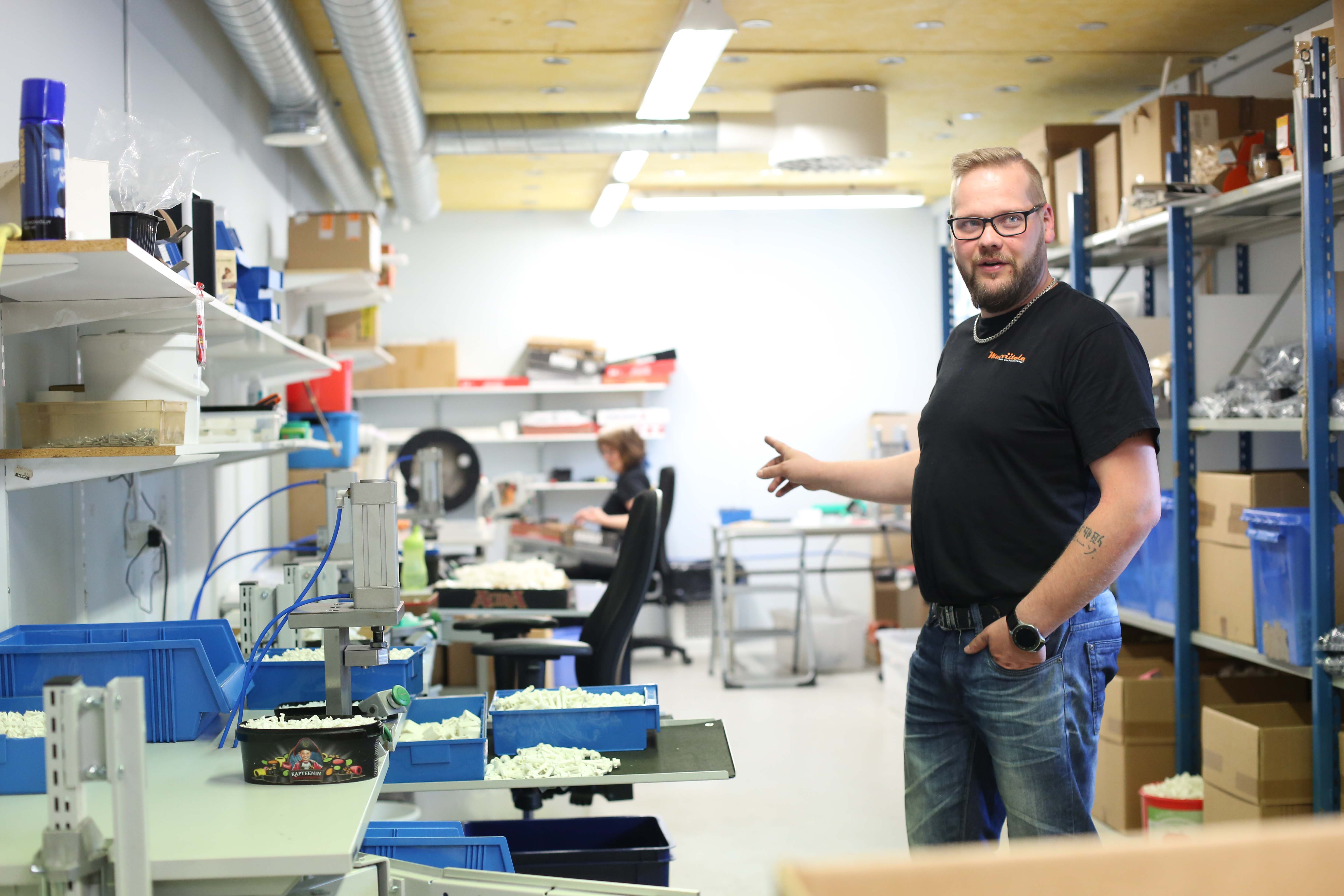Muoviitala-yrityksen yrittäjä Antti Viitala esittelee tuotantotiloja. Pöydillä valmiita tuotteita kokoonpanoa varten. Taustalla työntekijä kokoaa sälekaihtimien komponentteja. 