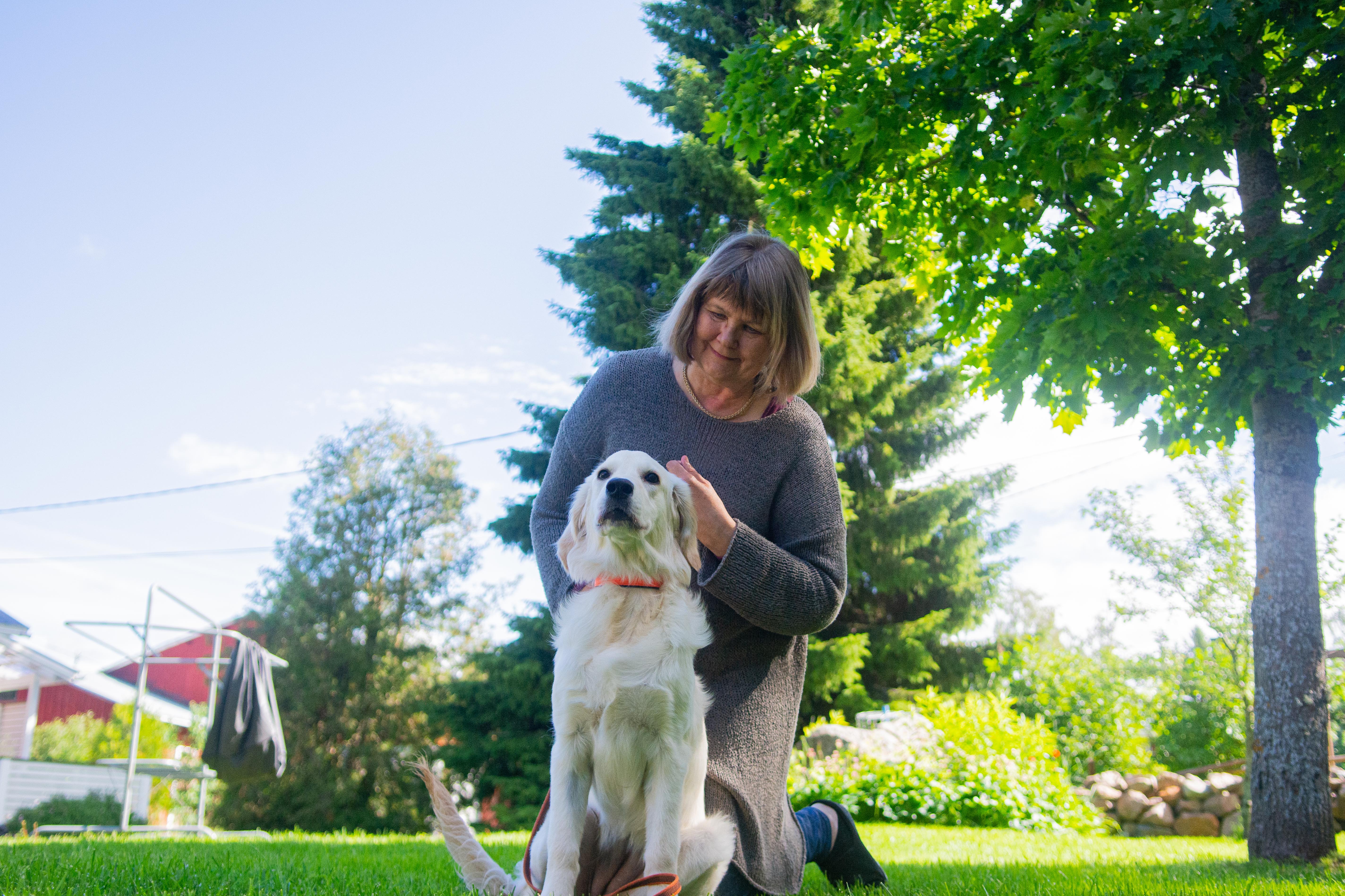 Kuvassa Aira Nissilä poseeraa ulkona nurmikolla koiransa kanssa. 
