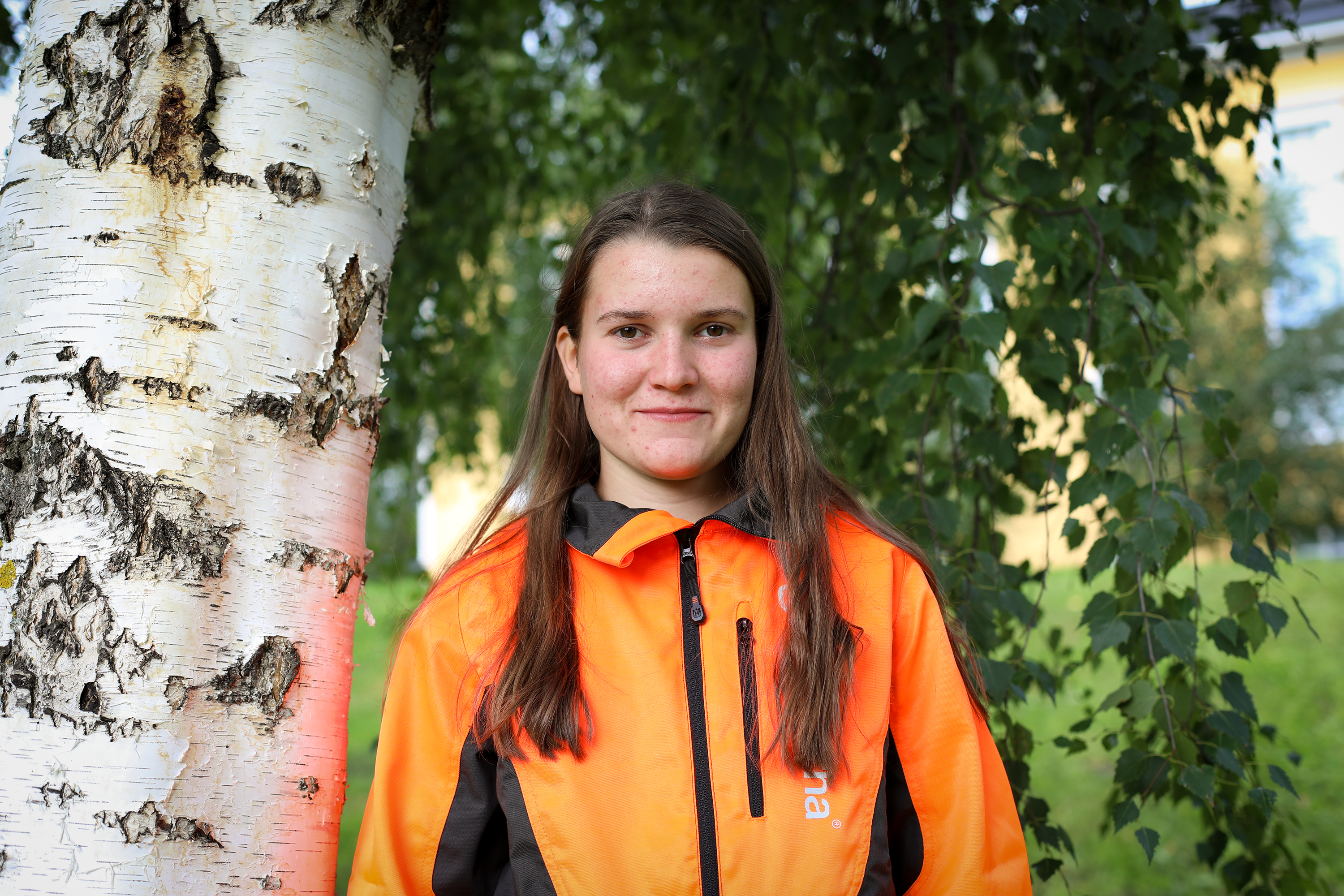 Kuvassa metsäalan opiskelija Katariina Rautio poseeraa koivuun nojaten päällään metsurin varusteet. 