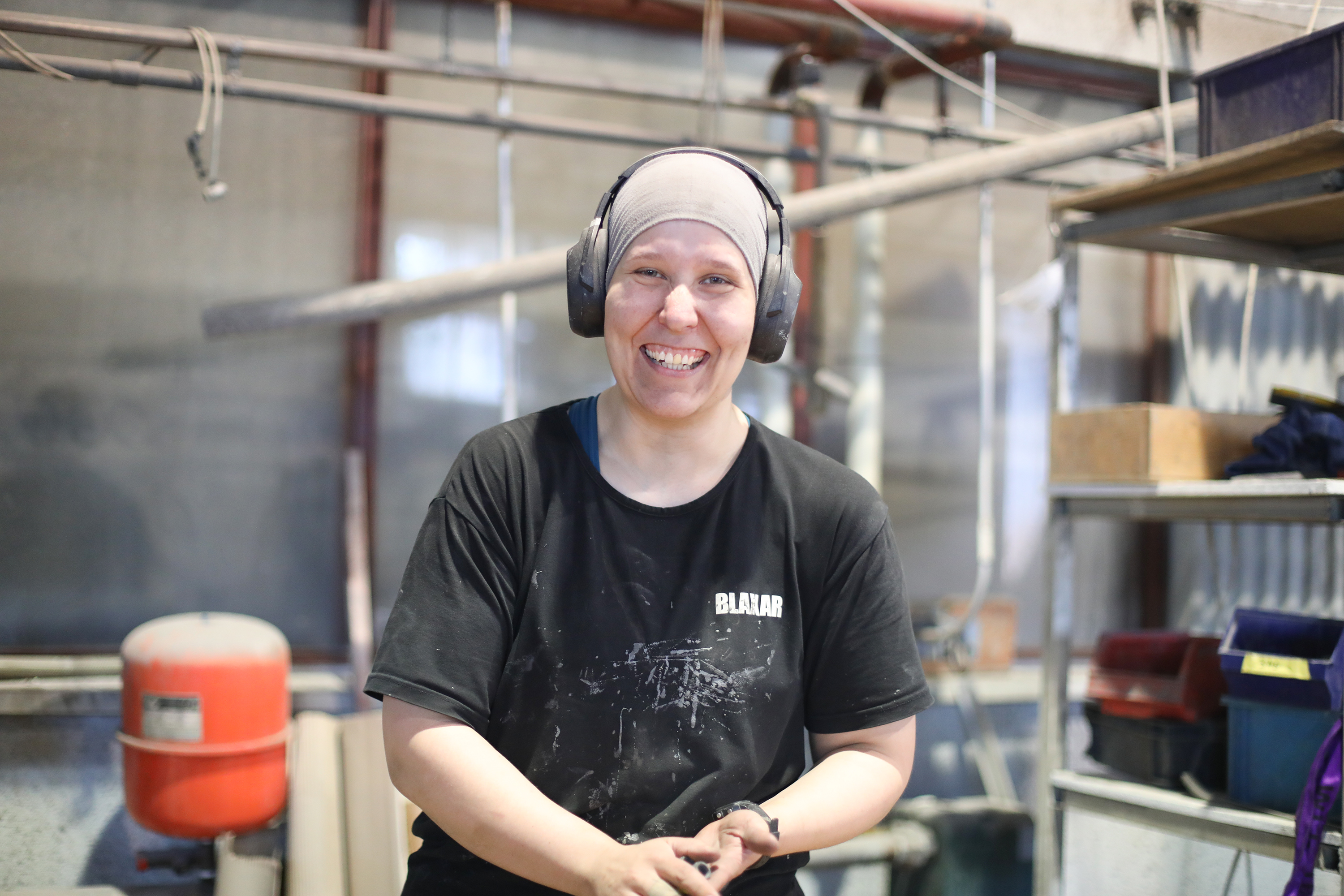 Kuvassa Blaxar Oy:lle työllistynyt Leena Alasirniö poseeraa tuotantohallin sisällä kameralle hymyillen. 