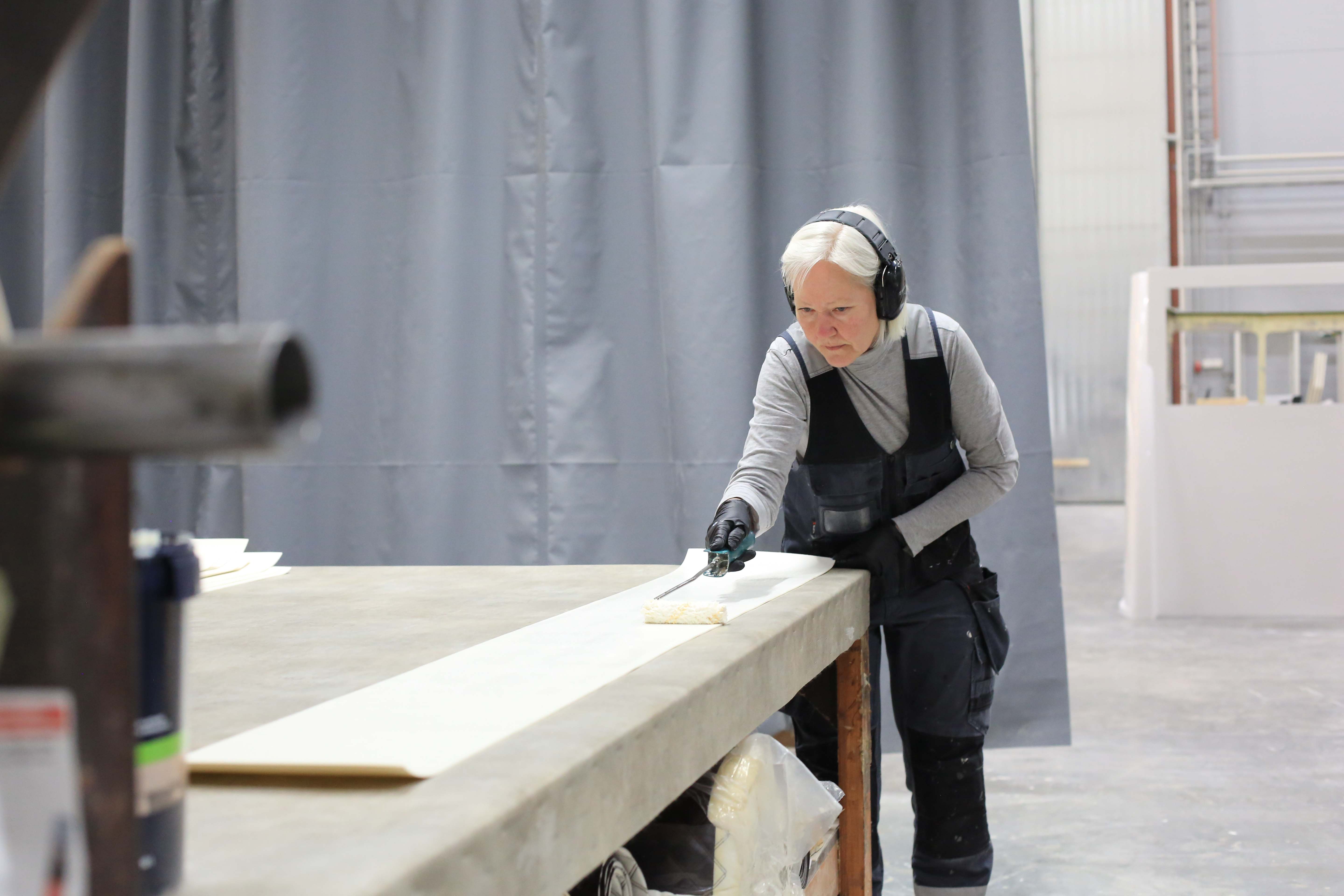 Kuvassa työntekijä Marjo Okkonen poseeraa tuotantohallissa töitä tehden. 
