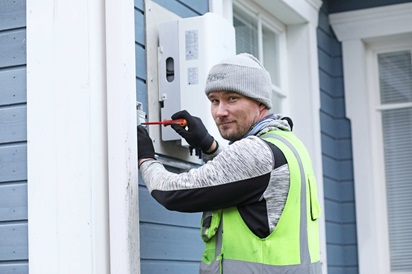 Kuvassa sähköalan yrittäjä Ville Linna poseeraa talon ulkopuolella sähkökaappia samalla ruuvaillen.