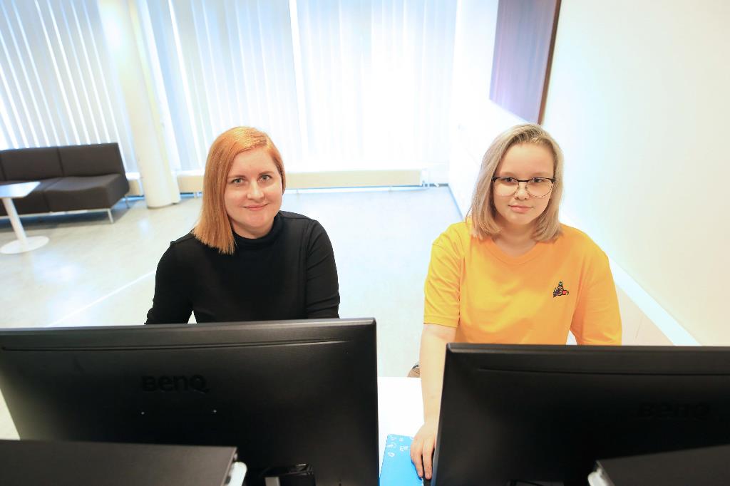 Kuvassa datanomiksi opiskelevat Yuliia ja Aada poseeraavat tietokoneiden ääressä istuen. 