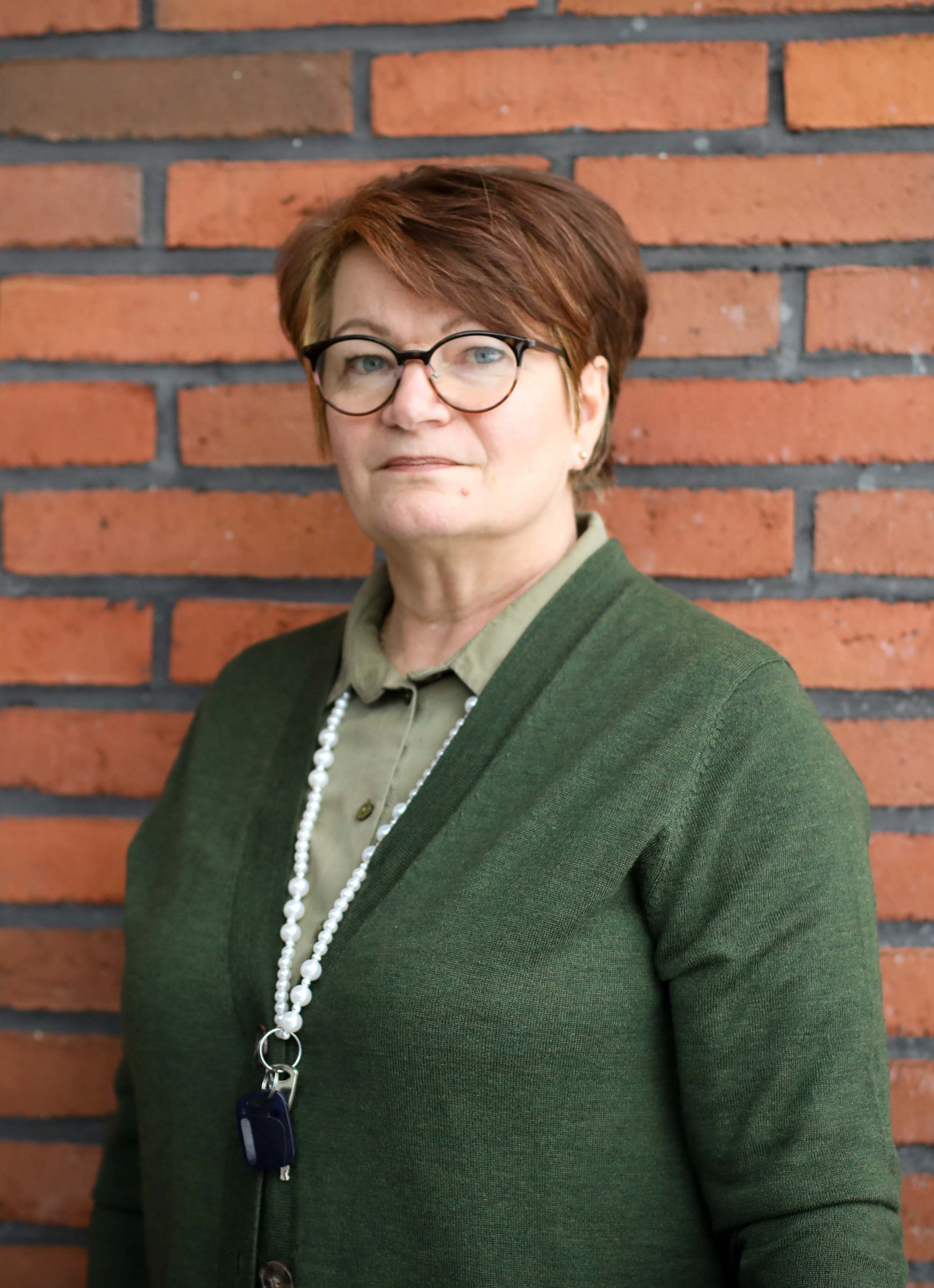 Kuvassa tiiliseinää vasten poseeraa opettaja Eeva-Maija Kiiskilä