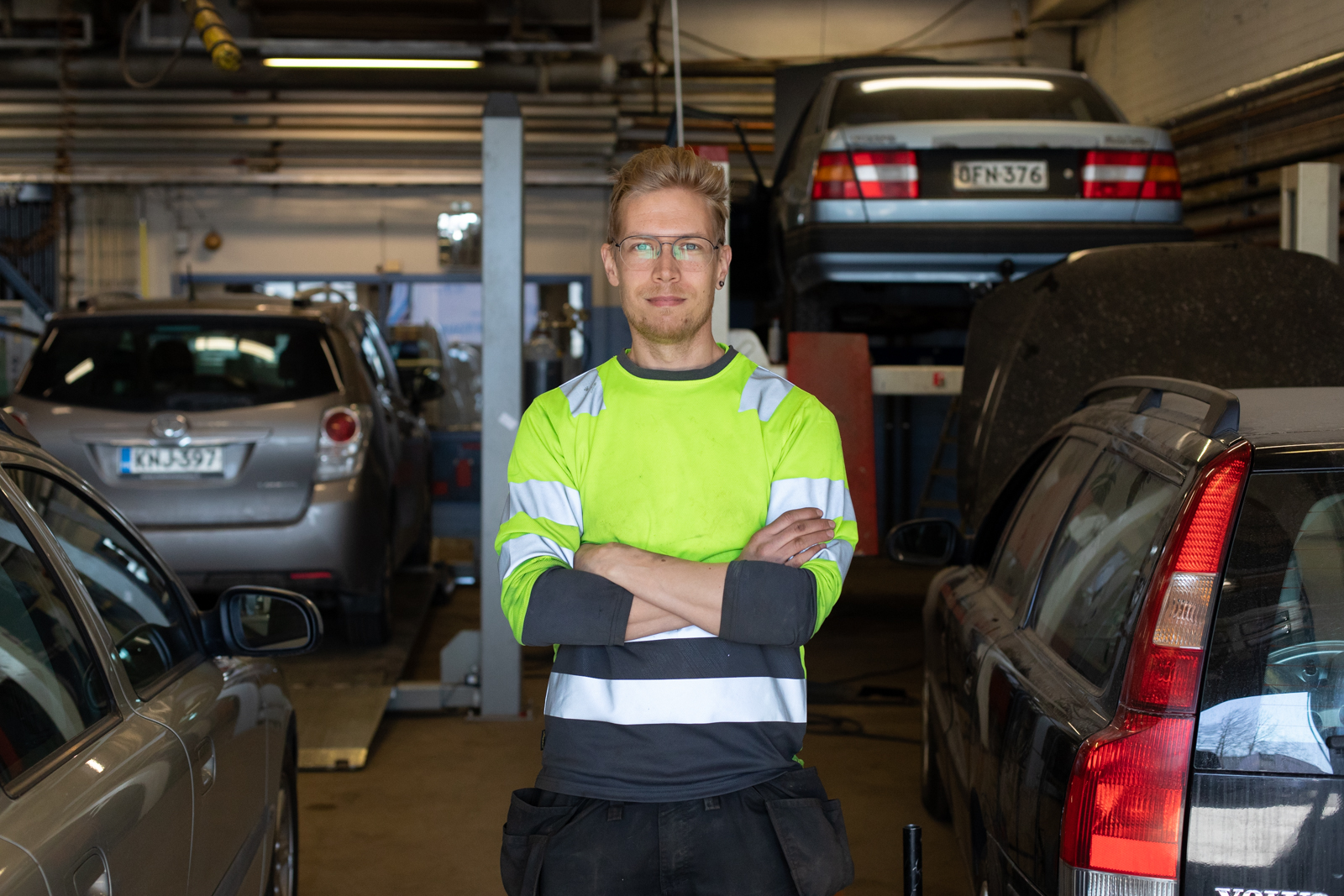 Kuvassa opettaja Markus Isohanni seisoo työvaatteissa autokorjaamossa autojen keskellä.