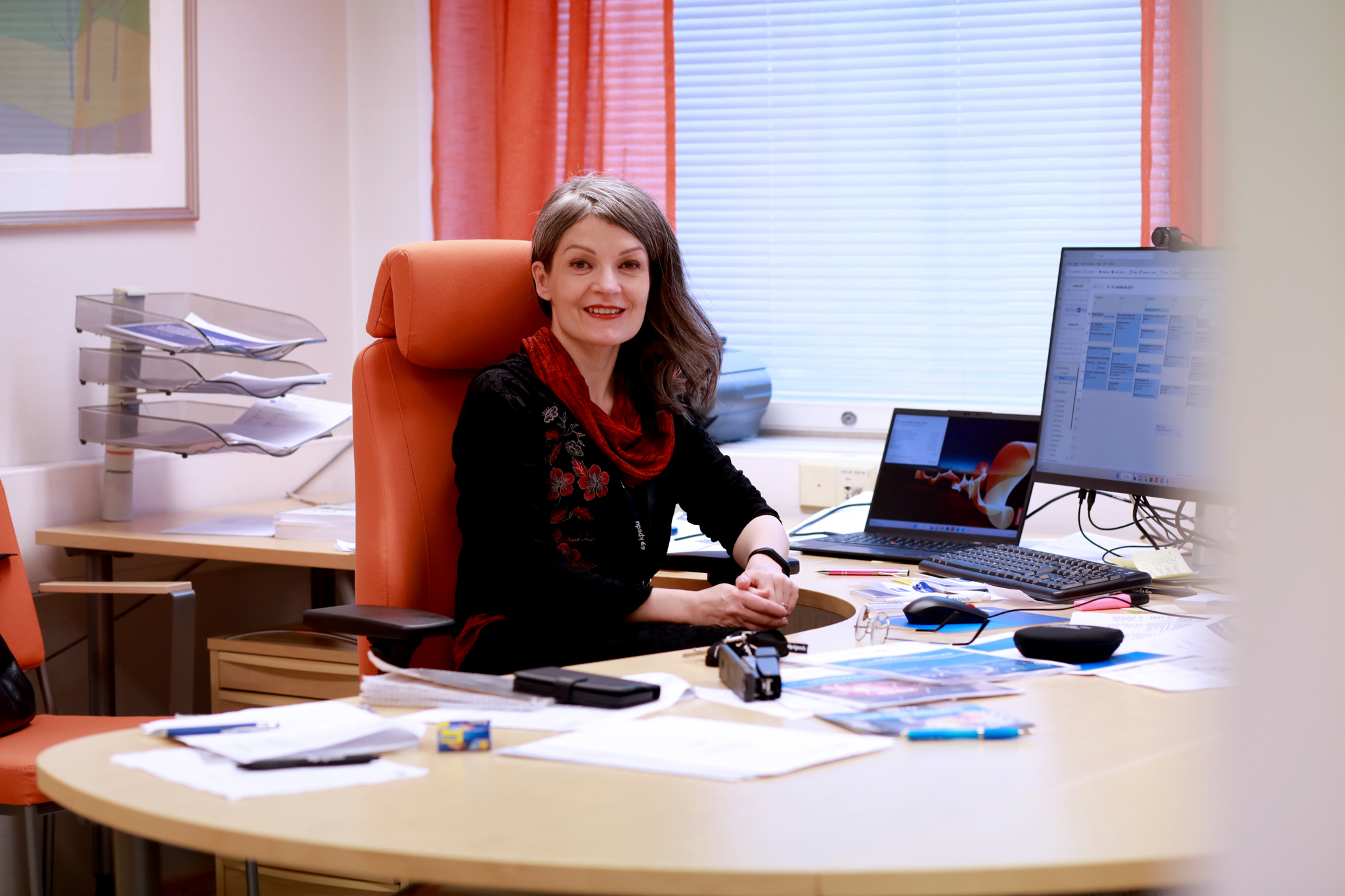 Kuvassa rehtori Nina Ollila poseeraa työhuoneen pöydän äärellä istuen. 
