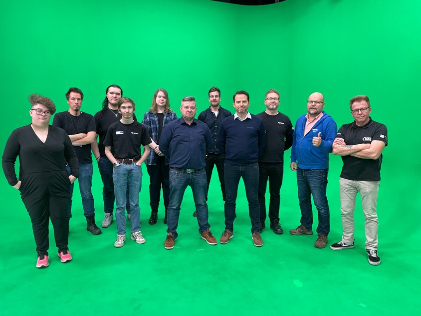 Työryhmä katsoo suoraan kameraan green screening edessä